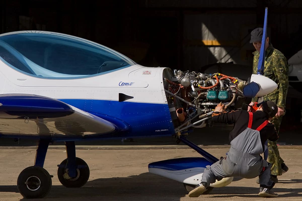 Technicians working on the exposed engine of a light aircraft